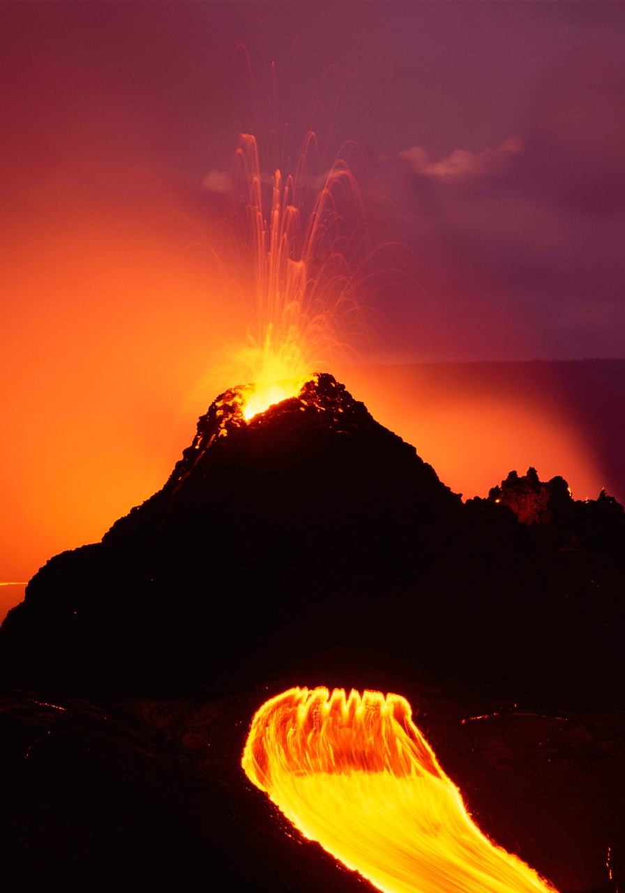 The cone of the Kilauea Volcano, the most active on Earth, erupts from the top while lava flows from the side in this photo by Brad Lewis.