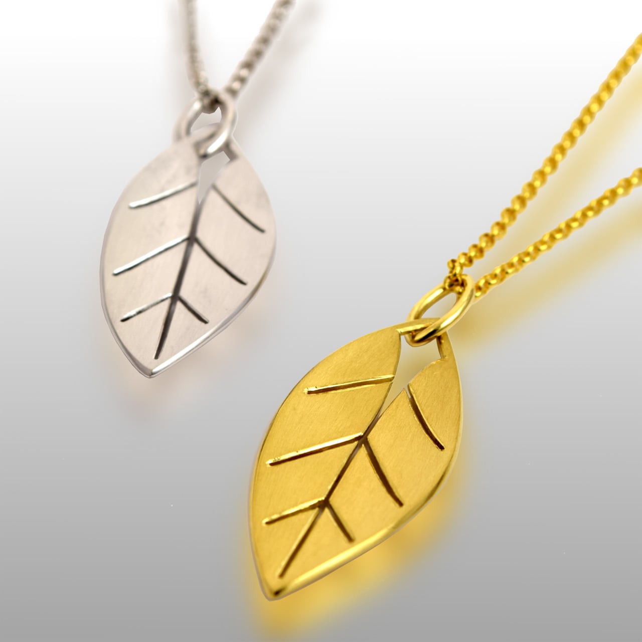 Two leaf pendants - one made of white gold and one made of yellow gold