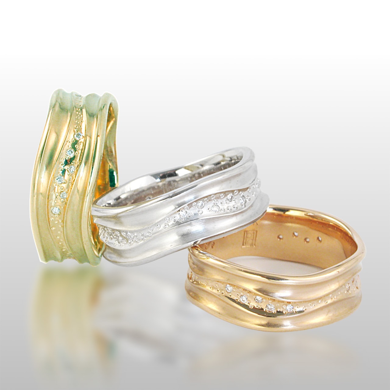 three wide band rings - one in yellow, white and rose gold. Curvy lines and diamonds set in the center