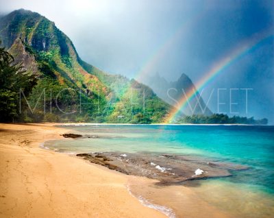 A double rainbow touches the Kauai coast in Hawai'i in this photo by Michael Sweet. Lush, rippled mountains are visible in the background.