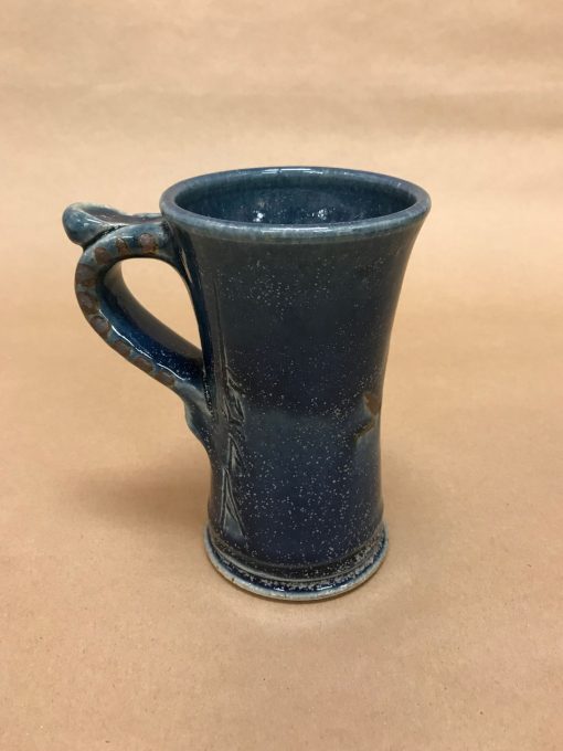 tall ceramic mug with a thumb rest. Blue hues, mostly deep navy colored.